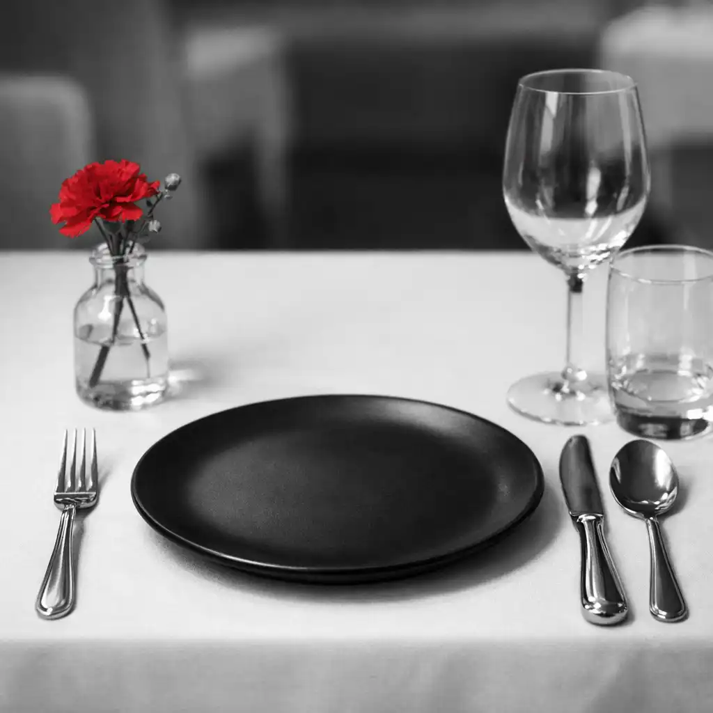 Close-up of an elegant table setting with a white tablecloth, black plate, polished silverware, and a small red flower